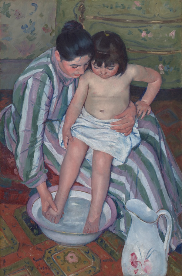 An adult washes a child in a patterned interior with a bowl and rug.